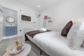 Ein modernes Schlafzimmer mit einem Bett, einem Nachttisch mit Tablett, einem Spiegel, einem Kleiderschrank, einem an der Wand montierten Fernseher und einem Regal mit Handtüchern.