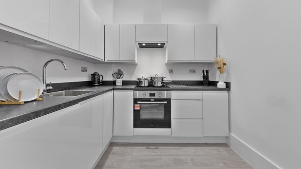 Una cocina moderna con armarios blancos, encimera negra, electrodomésticos de acero inoxidable y un pequeño comedor con una mesa redonda y sillas.