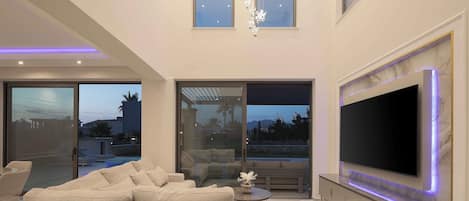 A modern living room with a large flat-screen TV, a sofa, and a glass door leading to an outdoor area.