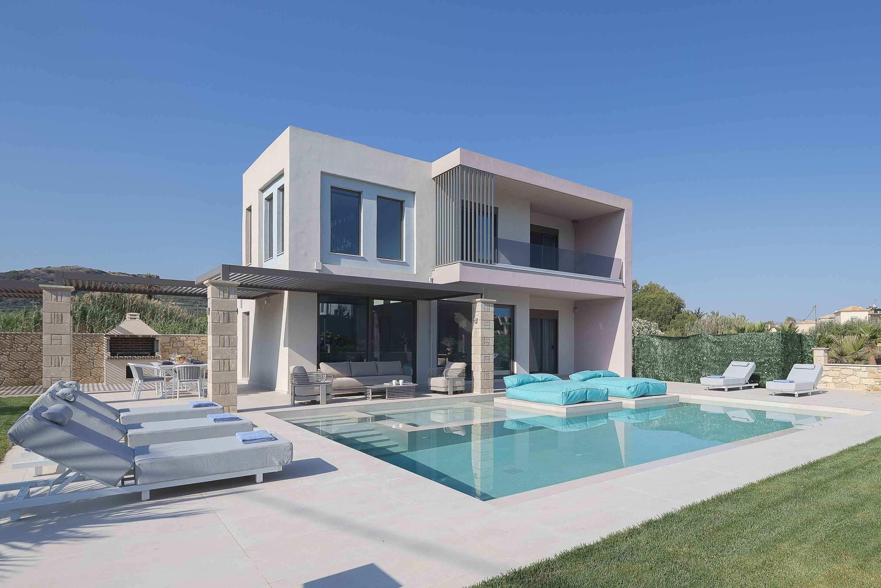 A modern two-story house with a swimming pool, outdoor seating, and a stone wall.