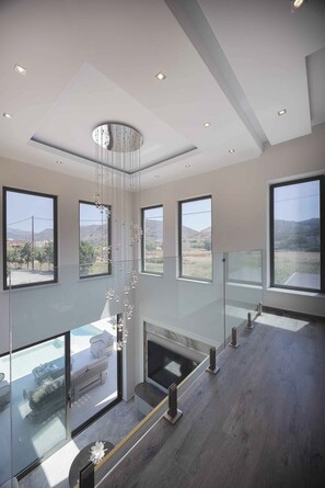 A modern interior with large windows, a central light fixture, and a seating area with a view. - Atriora Luxury Villa – Holiways Collection (Chania)