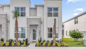 A modern two-story residential building with a stone facade, multiple windows, and a well-maintained front yard with various shrubs and a palm tree. - Luxury  House 4 Bedroom Family, Private Pool (Clermont)