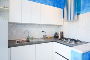 A modern kitchen with white cabinets, a stainless steel sink, a gas stove, and a blue backsplash. - Pietra Ligure | Pietra Ligure House (Pietra Ligure)