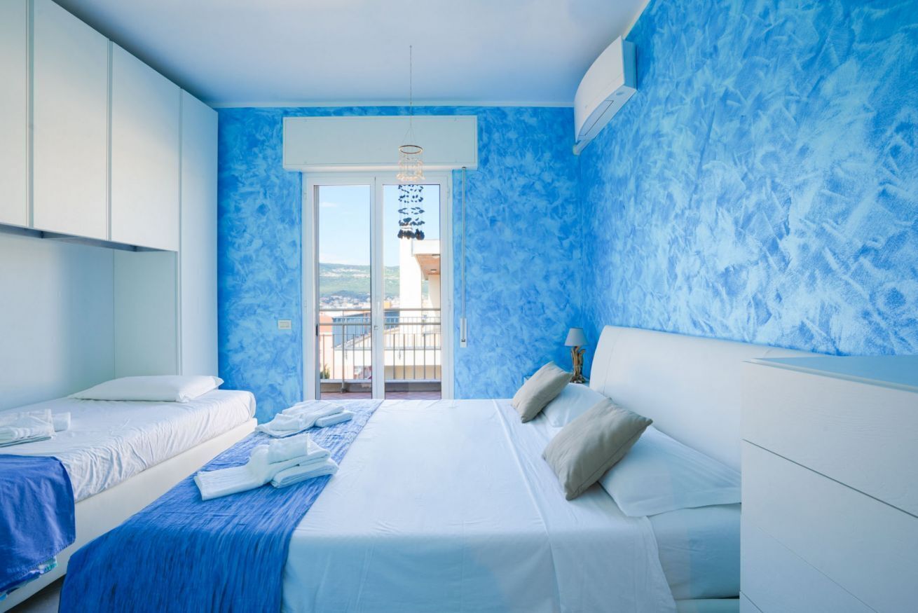 A bedroom with two beds, a balcony, and a view of the city.
