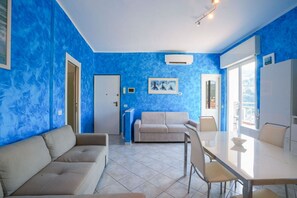 A room with a blue wall, a beige sofa, a white table, and a door. - Pietra Ligure | Pietra Ligure House (Pietra Ligure)
