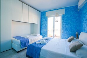 A hotel room with a large bed, two smaller beds, a balcony, and a view of the outdoors. - Pietra Ligure | Pietra Ligure House (Pietra Ligure)