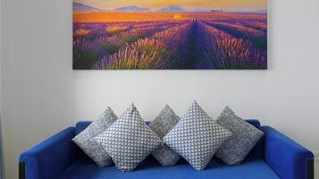 A blue sofa with patterned pillows and a landscape painting above it.