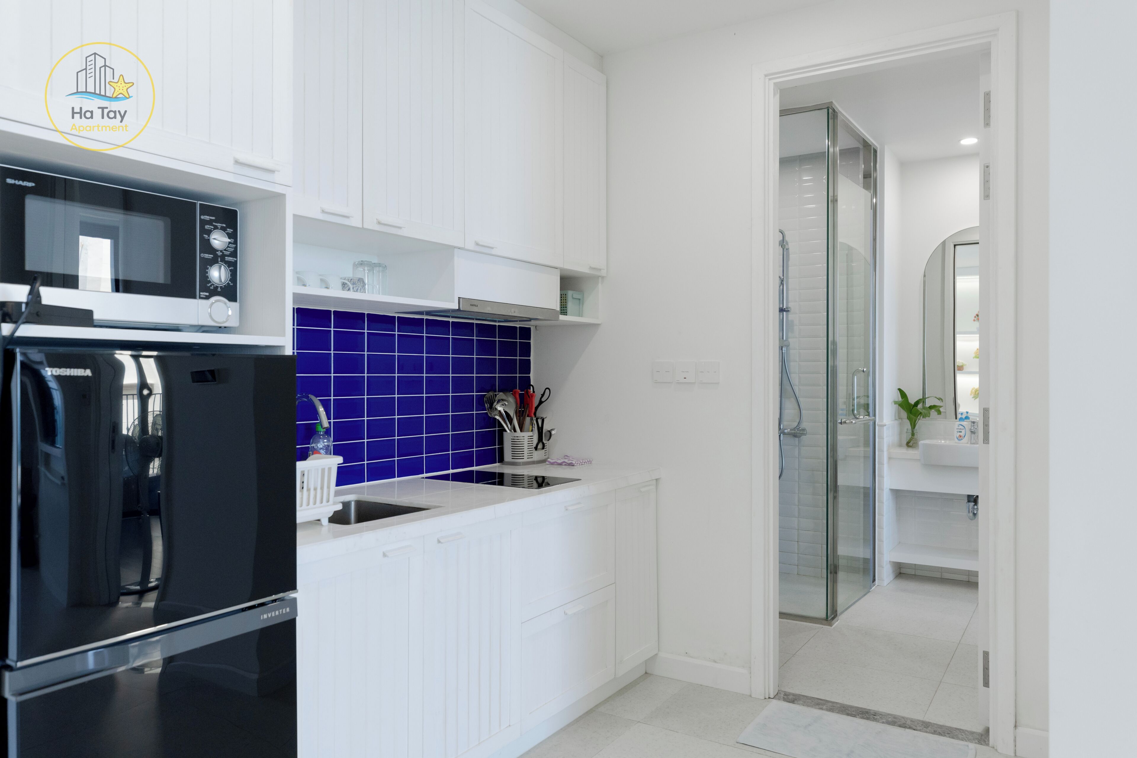 A modern kitchen with white cabinets, a blue backsplash, and a glass-enclosed shower.