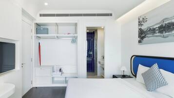 A modern hotel room with a bed, a TV, a wardrobe, and a bathroom visible through an open door.