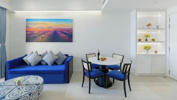 Un salon moderne avec un canapé bleu, une table de salle à manger ronde entourée de chaises, un tableau représentant un paysage et une étagère blanche agrémentée d’objets décoratifs.