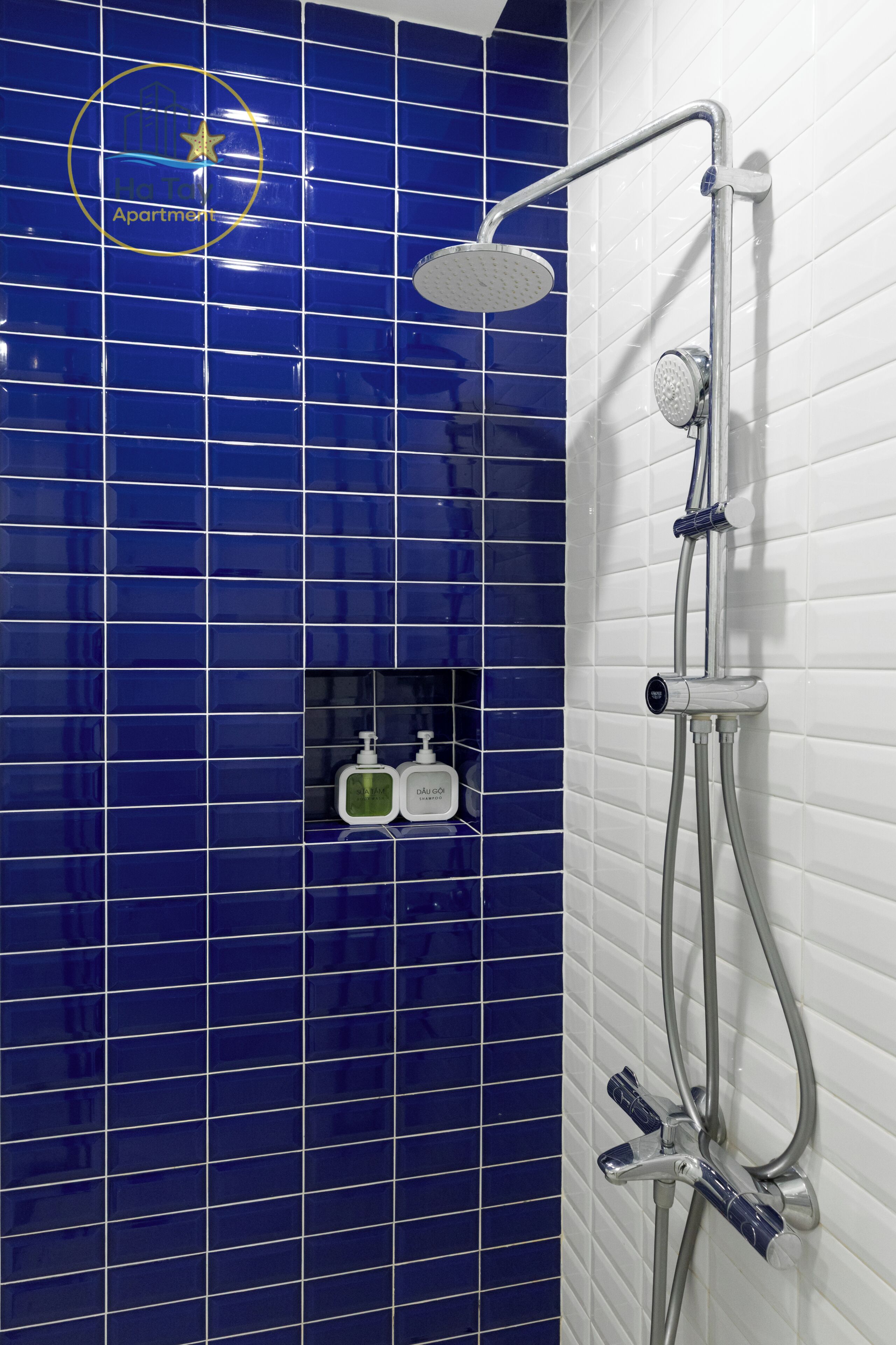 A bathroom with blue tiles, a shower, and two bottles of hand soap.