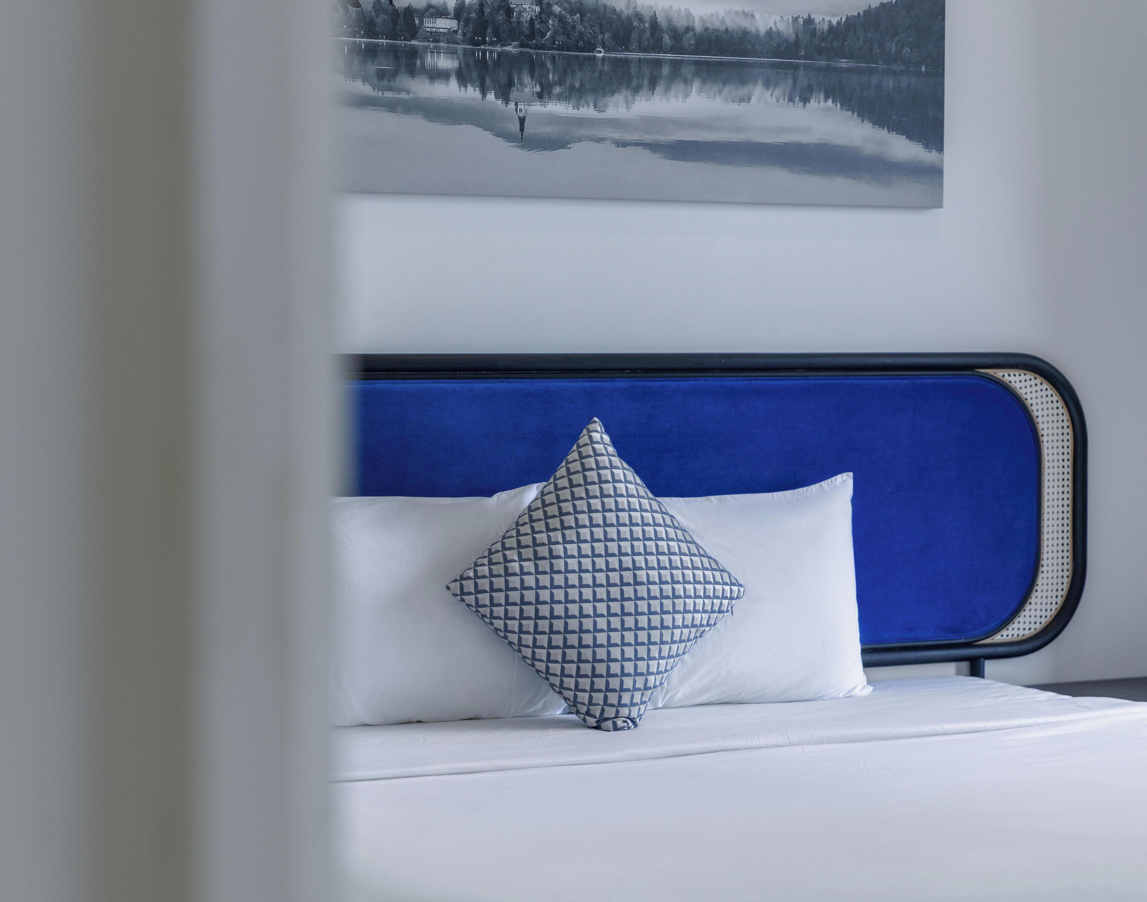 A bed with a blue headboard, white bedding, and a patterned pillow.