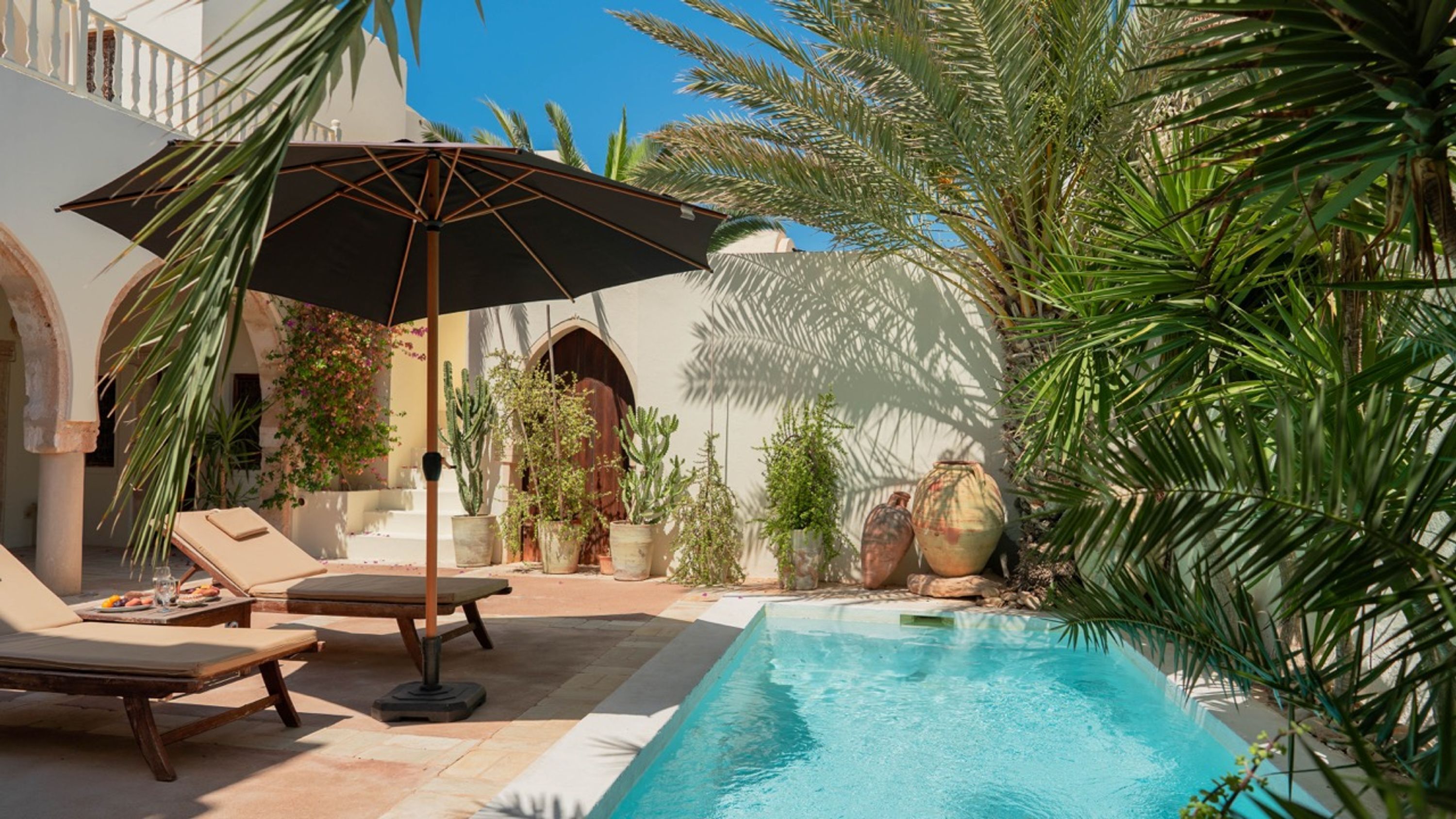 A poolside area with lounge chairs, a table with a drink, and a large umbrella.
