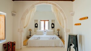 A bedroom with a canopy bed, two bedside tables with lamps, a window with a view, and decorative wall art. - Dar Meryem Djerba: Houch avec piscine (Djerba Midun)