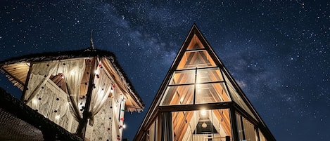 Two triangular glass-roofed structures with visible interior lighting and a starry night sky.