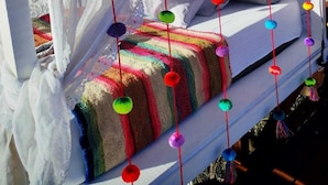 Una cama con almohadas coloridas y un edredón a rayas, bajo un dosel con detalles decorativos colgantes.