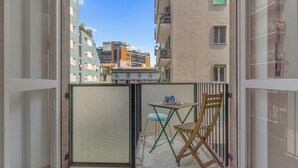 En balkon med et bord og stole, udsigt til omkringliggende bygninger, og en nettingskærm.