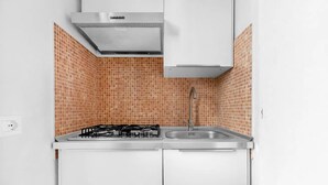 Una cocina con estufa a gas, pileta de acero inoxidable y alacenas blancas.