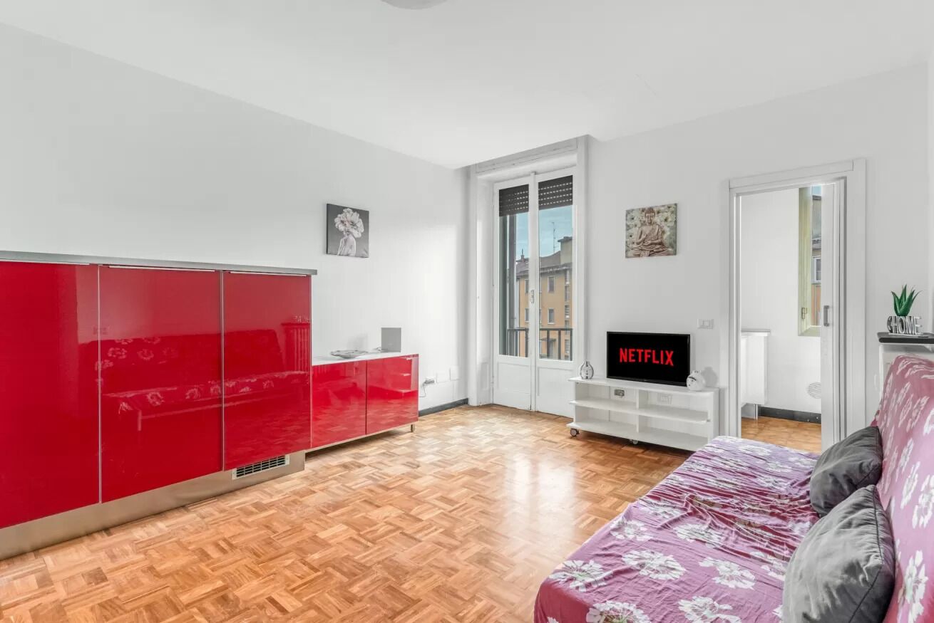 Una camera moderna con pavimento in legno, un armadio rosso, un mobile TV bianco e un letto con copripiumino floreale.