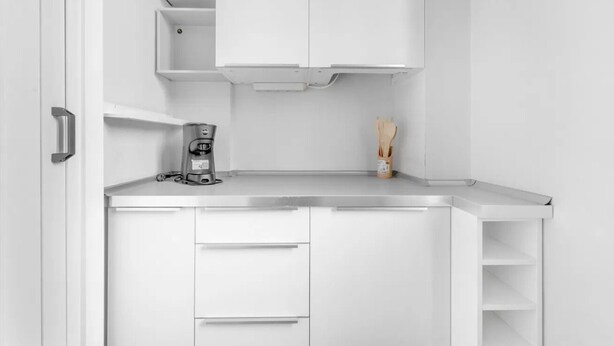 Cocina compacta con armarios blancos, cafetera y un recipiente para utensilios.