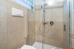 Ein modernes Badezimmer mit Duschkabine aus Glas, Waschbecken in Weiß und einem sichtbaren Lichtschalter an der Wand.
