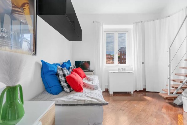 A modern bedroom with a bed, pillows, a TV, a window with curtains, and a staircase.