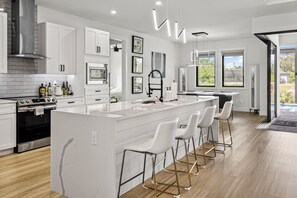 A modern kitchen with a central island, white bar stools, and a large window providing natural light. - Luxury Relaxing Waterfront House - Heated Pool - 4BD - Family and Pets Friendly (Port Charlotte)