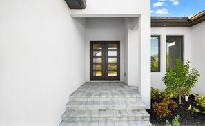 A modern house entrance with a double door, a set of steps leading up to it, and a small garden area with various plants. - Luxury Relaxing Waterfront House - Heated Pool - 4BD - Family and Pets Friendly (Port Charlotte)