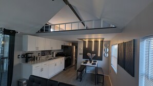 Eine moderne Küche mit weißen Schränken, ein Essbereich mit Tisch und Bänken sowie ein schwarzes Sofa.