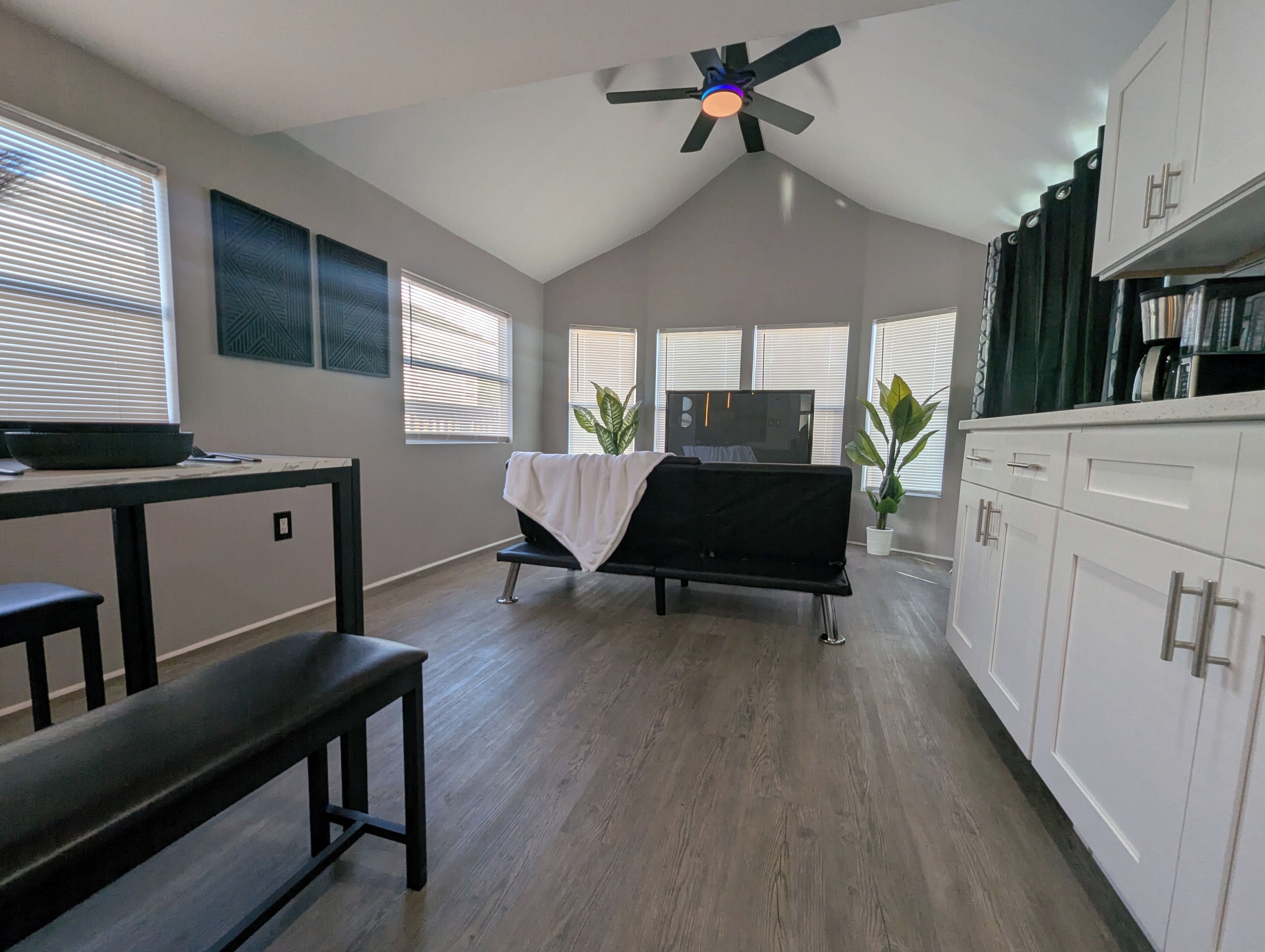 Un espacio habitable moderno con ventilador de techo, un sof á negro, una mesa de comedor y una cocina con armarios.