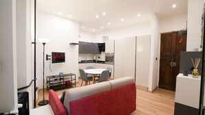 Un espace de vie compact comprenant un coin cuisine, un coin repas et un canapé rouge.