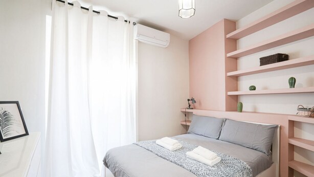 Une chambre à coucher comprenant un lit, une table de chevet, une étagère avec des objets décoratifs et un appareil de climatisation.