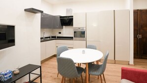 Une cuisine compacte avec un coin repas, comprenant une table ronde avec des chaises, un téléviseur noir et un four à micro-ondes.