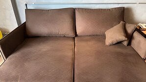 Um sofá marrom com uma almofada e um telefone num apoio lateral.