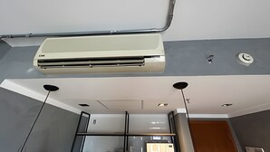 Quarto de hotel moderno com um ar condicionado grande fixado no teto, porta visível e divisória de vidro.