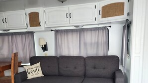 A grey sectional sofa with a matching grey rug, a wooden chair, a small table, and white cabinetry above.