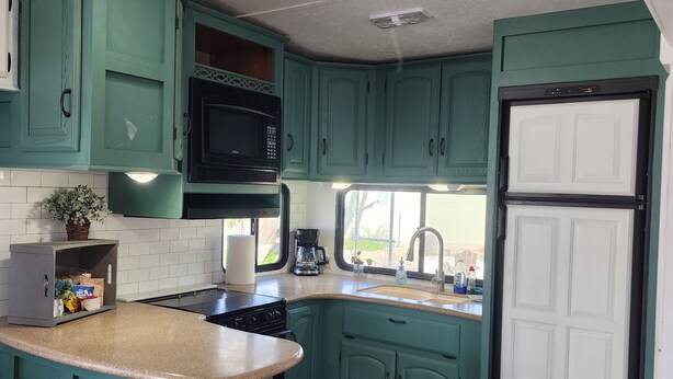 A compact kitchen with teal cabinetry, a microwave, a coffee maker, and a refrigerator.