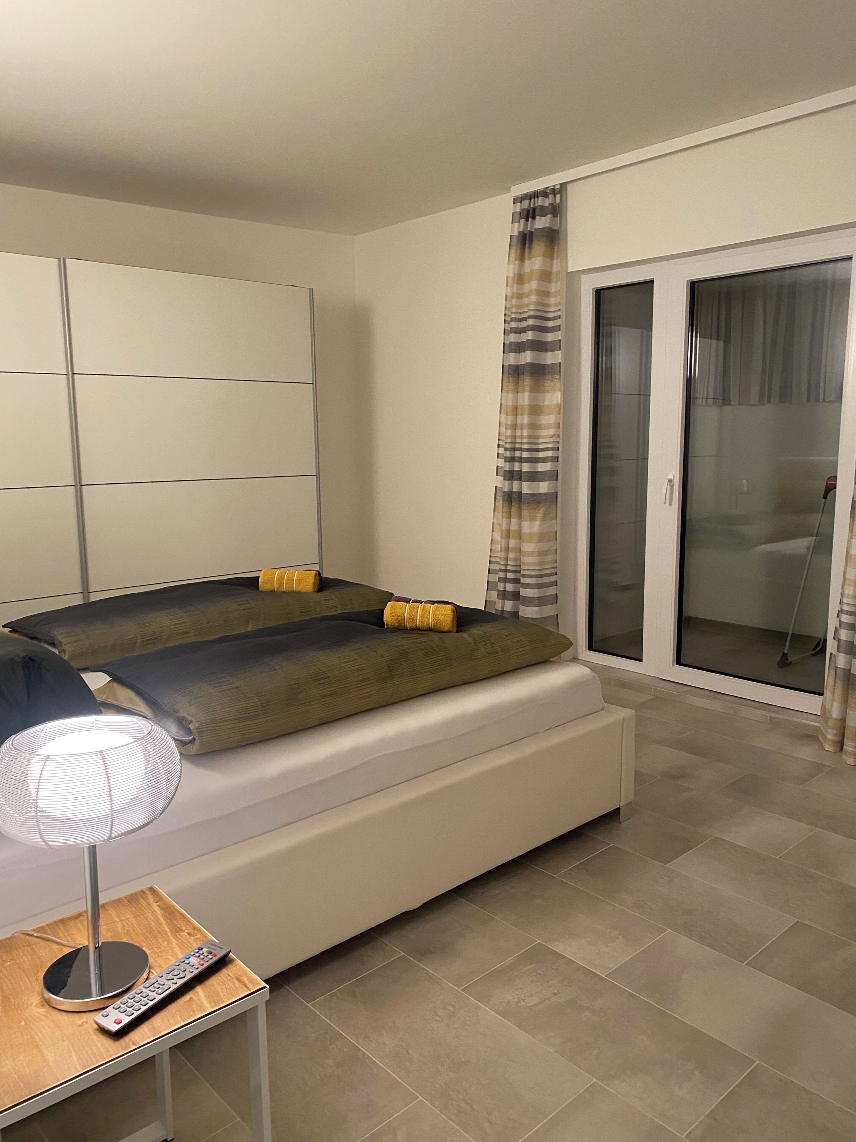 Une chambre moderne avec un lit, une table de chevet avec une lampe et une porte-fenêtre coulissante donnant sur un balcon.