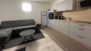 A compact living space with a sofa, a small round table, a kitchenette with a microwave, and a refrigerator. - Vacation rental for 4 people, about 2.5 km from the center (Villach)