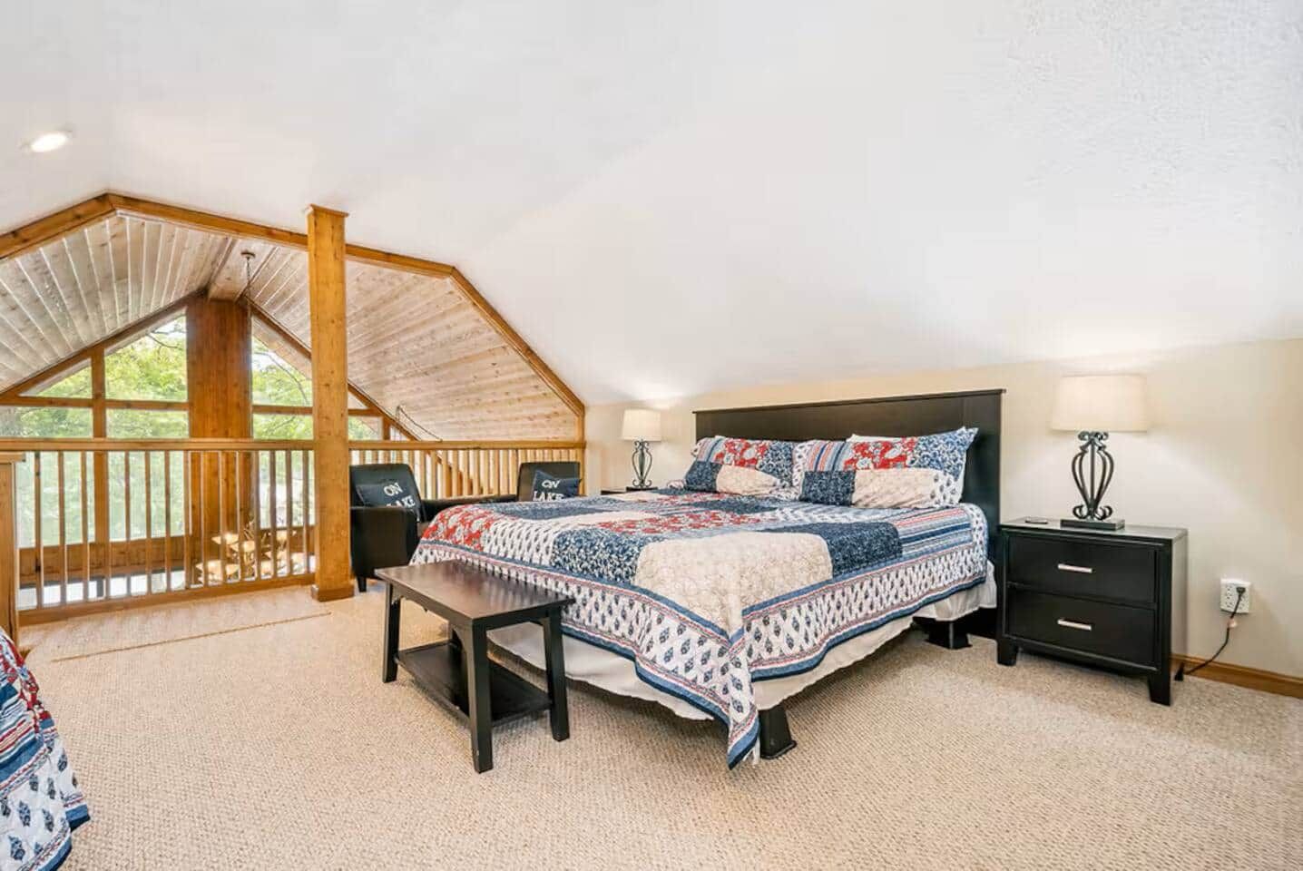 Une chambre à coucher avec un grand lit, une table de chevet, un banc et une vue sur l’extérieur par une fenêtre.