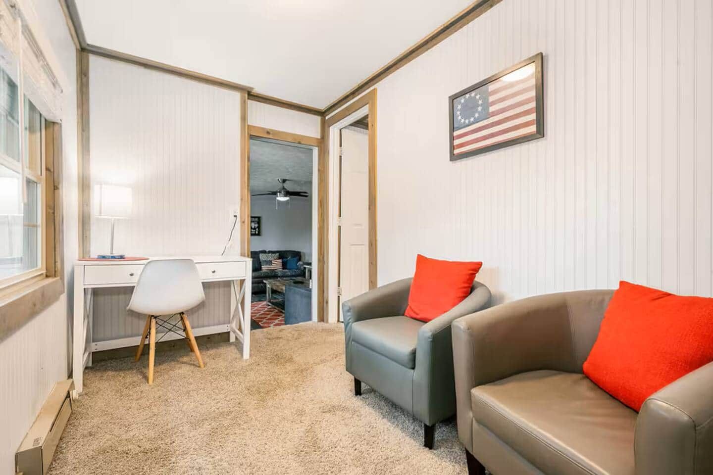 A room with a desk, two leather sofas with red cushions, a small chair, and an American flag on the wall.
