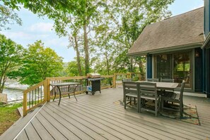 Eine Holzterrasse mit Tisch, Stühlen, einem Grill und einem Mülleimer.