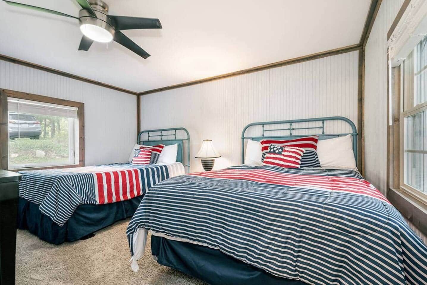 A bedroom with two beds, each with a striped bedspread, a ceiling fan, and a window.