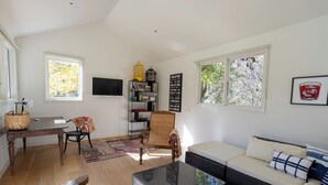 A living room with a sofa, a coffee table, a TV, a bookshelf, and a window with a view of trees.