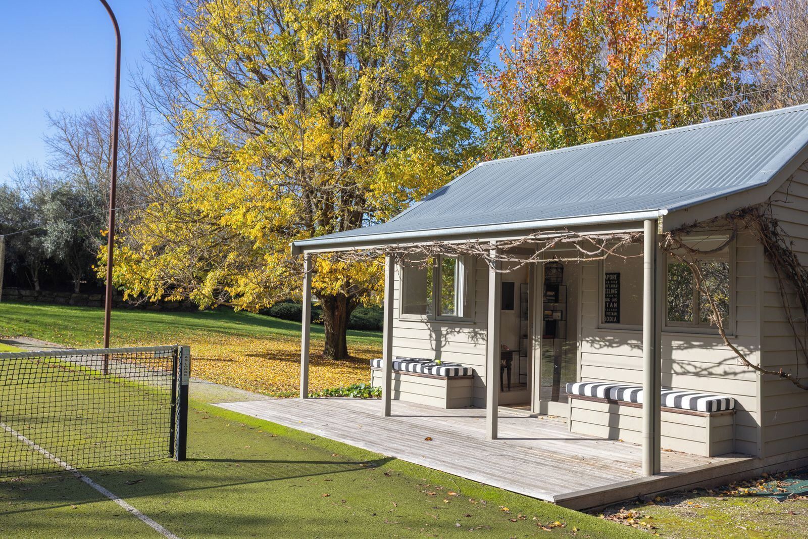 A small pavilion with a roof, benches, and a tennis court in the background.