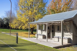 A small pavilion with a roof, benches, and a tennis court in the background.