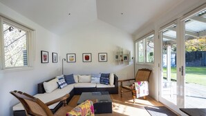 A modern living room with a sectional sofa, wooden chairs, a coffee table, and a large sliding glass door leading to a garden.