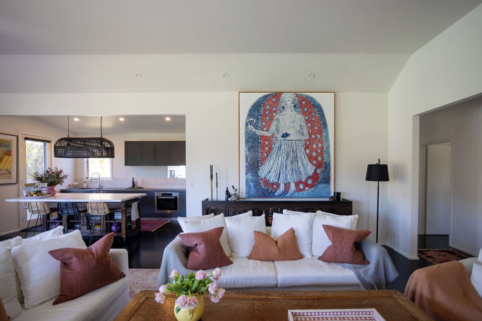 A modern living room with a sofa, a coffee table with flowers, and a large abstract painting above the sofa.