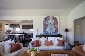 A modern living room with a sofa, a coffee table with flowers, and a large abstract painting above the sofa.