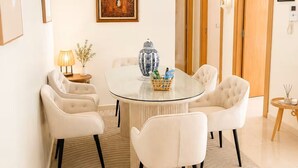Un comedor con una mesa de vidrio rodeada por cuatro sillas, un florero y una lámpara sobre una mesita auxiliar.